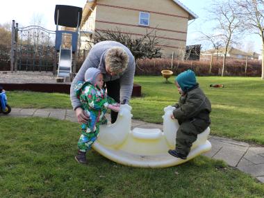Dagplejemor, som hjælper lille barn med at holde balancen på vippen - legeplads